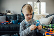 © Cavan Images - Close up of small boy wearing headphones in front of messy couch