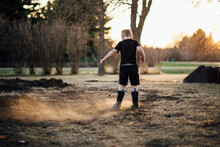 Wide Read View Of Young Boy Kicking Up Dirt In Yard On Hazy Summer Eve