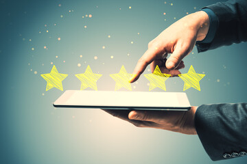 Close up of businessman hand pointing at tablet with 5 star rating on blurry background. Customer service and excellent feedback concept.