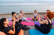 Top view of group of young-adult multi-racial women are sitting on sports mats and talking and applaud each other. Concept of female circle of communication and outdoor yoga class