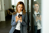 Fototapeta Przeznaczenie - Smiling Businesswoman in Modern Office Holding Smartphone Enjoying a Successful Work Day