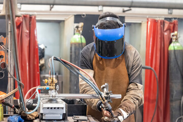 A masked worker is fully immersed in their welding task. Bright sparks fly as they focus intently on a specific point of the metal. The intense light illuminates their face