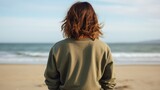 Fototapeta Pokój dzieciecy - Back view of a girl with wavy brown hair in plain olive crewneck sweatshirt mockup on a beach background with the ocean