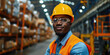 A warehouse worker wearing protective gear, a hard hat and a reflective vest stands in a large industrial warehouse.