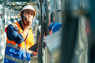 Wall Mural - Professional Asian man engineer in safety uniform working on digital tablet at outdoor construction site rooftop. Industrial technician worker maintenance checking building exterior air HVAC systems.