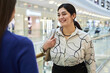 Waist up portrait of smiling Middle Eastern woman talking to friend in shopping mall and smiling