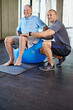 © peopleimages.com - Physiotherapist, portrait and senior man with ball, training and elderly support for care. Men, gym and exercise for health, wellness and coaching with arthritis for mature rehab and wellbeing