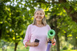 © Liubomir - Portrait of a smiling senior active woman holding a mat, a phone and a bottle of water in her hands. Standing in the park and confidently looks into the camera.