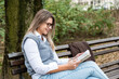 © Srdjan - Young successful business woman sitting in the park on the bench reading a book on a break from work.