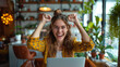 © T-elle - Joyful young woman celebrating success in a cozy cafe with a laptop