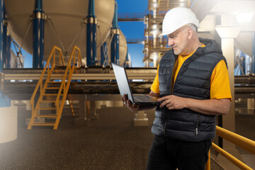 Poster - man industrial engineer. industrialist near chemical factory. engineer stands with laptop in his han