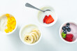assortment of different yogurts with berries, fruits, mango and banana on white. healthy breakfast