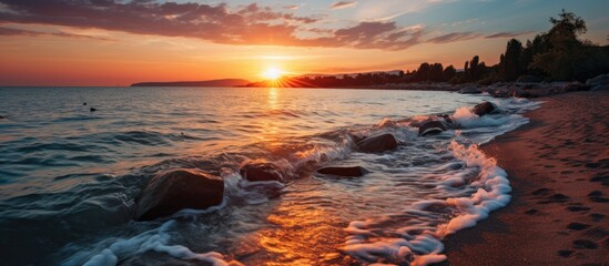 Wall Mural - A serene sunset captured at the meeting point of a river and the sea, showcasing beautiful rocks and gentle waves under the colorful sky