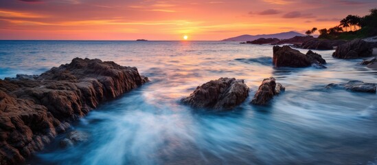 Aufkleber - Scenic view of a beautiful sunset over the ocean, with rocks scattered along the shoreline and waves crashing gently