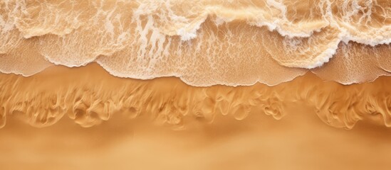 Poster - View from above of a beach with sand as the background and a wave rolling towards the shore