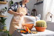 Repotting overgrown home plant large spiny cactus Echinocactus Gruzoni into new bigger pot. A woman in protective gloves wraps a cactus with a bubble wrap so as not to prick herself