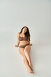 © LIGHTFIELD STUDIOS - pretty plus size young woman in brown underwear sitting and leaning to arms on grey background