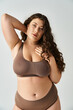 charming plus size woman in underwear with brown hair putting hand behind head and touching neckline