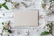 Delicate white flowers scattered around a blank card on rustic wood