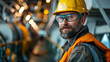 A bearded worker in safety gear stands confidently in an industrial setting, showcasing workplace safety and professionalism.
