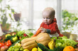 Small child examines fresh carrots among various vegetables and fruits. Healthy baby food concept.