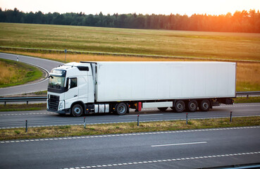 A modern truck with a refrigerator semi-trailer with refrigeration equipment transports flower products while maintaining the temperature regime against the backdrop of sunset and forest.