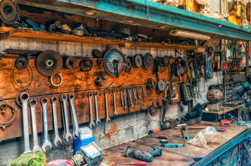 Old workshop with tools. Wrenches and grinding wheels hang on wall. Repair items on table and shelve