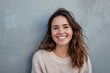 © SHOTPRIME STUDIO - Portrait of a young woman with a bright smile standing confidently in front of a monochromatic grey wall