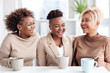 A trio of cheerful plump plus-size women chat happily while having coffee at the workplace, dressed in elegant outfits in a well-lit modern indoor office.