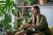 © DimaBerlin - Calm relaxed woman plant lover taking care about houseplants. Interested middle aged female have indoor plant hobby with green indoor plant monstera examines touching leaves sitting on floor at home.