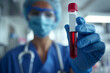 Healthcare professional in scrubs and protective gear holding a blood sample vial in a clinical setting