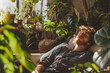 © Lewis - A ginger man sleeping on a couch in a room full of plants, relaxation and calm sunshine
