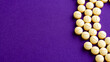 A bunch of pills are on a purple background. The pills are yellow and are arranged in a line