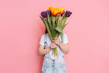 Fototapeta Maki - Little girl holding a bouquet of tulips in front of a pink background.