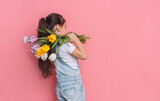 Fototapeta Maki - Little girl carries a bouquet of tulips on her shoulder against a pink background.