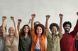 A diverse group of individuals lifting their hands together, set against a plain backdrop