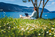 Young woman sitting on a green summer lawn on the seashore using a laptop