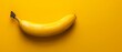   A yellow banana sits on a yellow table beside a yellow banana peel
