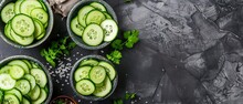   Cucumber slices are arranged in small bowls on a gray surface with a seasoning bowl nearby