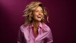 © mandu77 - A radiant woman with blonde hair laughs wholeheartedly against a deep purple backdrop, wearing a stylish pink shirt