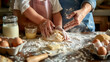 A pair of adult hands guides a child's hands in kneading dough on a flour-dusted wooden kitchen table surrounded by baking ingredients.