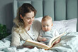 © romanets_v - Young mother reading book to her cute little baby on bed