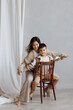 Caucasian mother and child in warm clothes share a tender moment. They sit next to each other on an antique chair against a light background. Concept: family connections, health.