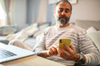 © Davor - Middle-aged man using smartphone at home