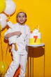 © saulich84 - photo session of a boy in a yellow hat and white T-shirt with a toy bird goose hugging standing on a yellow paper background in a studio. standing next to a cake with a goose on it