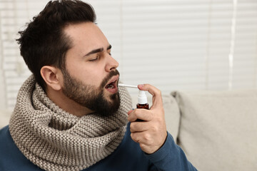 Canvas Print - Young man with scarf using throat spray indoors