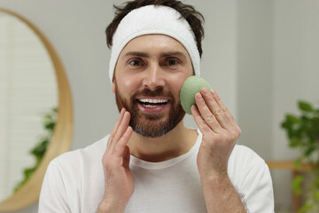 Wall Mural - Man with headband washing his face using sponge in bathroom