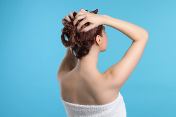 Wall Mural - Young woman washing her hair with shampoo on light blue background, back view