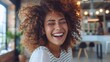 Portrait of beautiful young woman laughing at creative office. Happy businesswoman with curly hair excited with toothy smile. Enthusiastic cheerful girl looking at camera