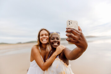 two friends having a good time on the beach taking selfie pictures with their smart phone during a summer trip